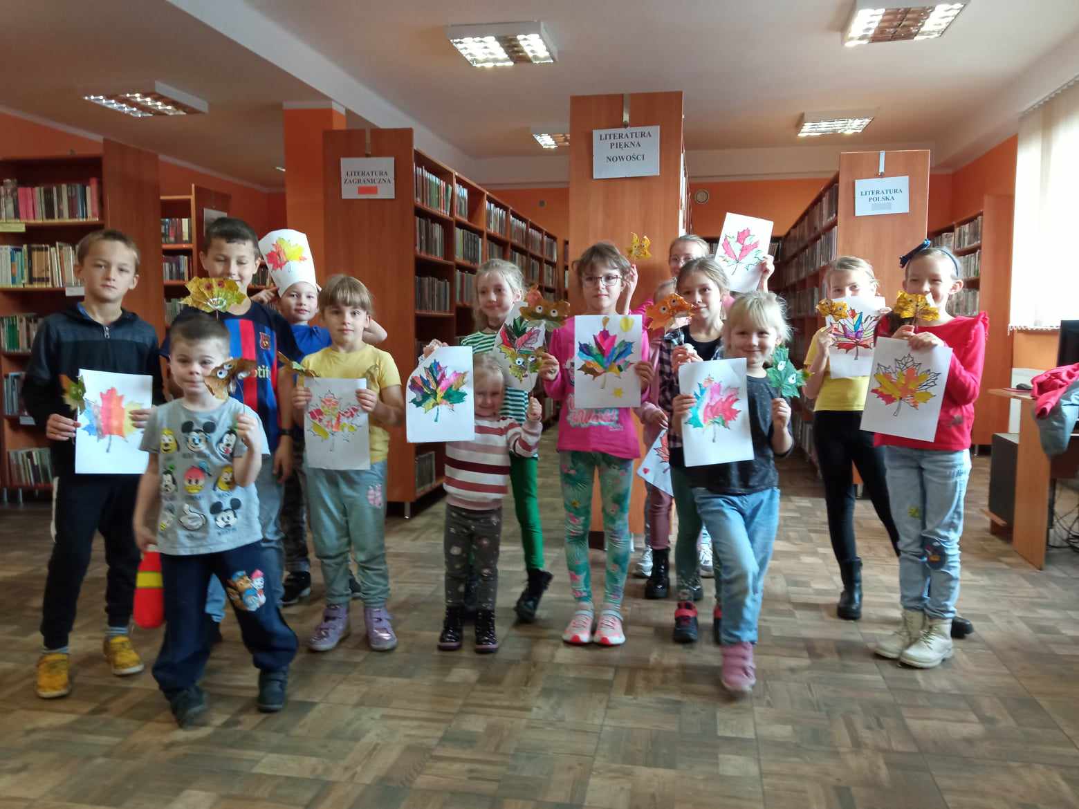 Dzieci w bibliotece prezentują prace plastyczne, narysowane kolorowe jesienne liście.