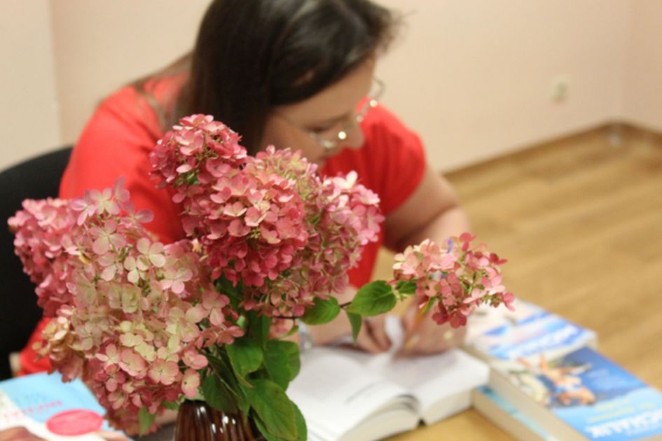 Kwiaty w wazonie, autorka podpisuje książkę przy stole