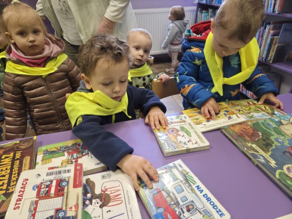 Dzieci w bibliotece przy stole z książeczkami dla dzieci. Czwórka dzieci ze żłobka.