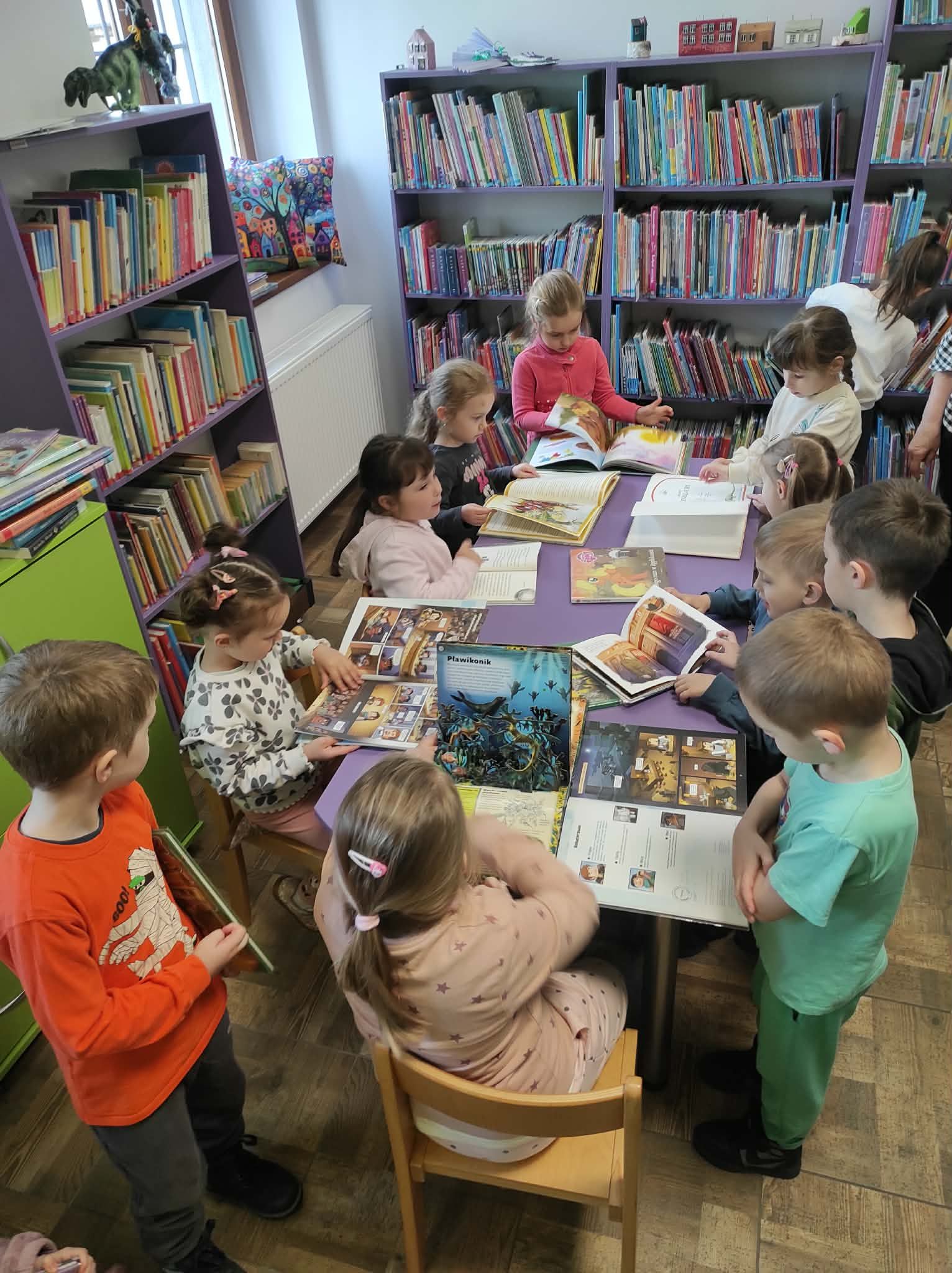 Dzieci z przedszkola w bibliotece przeglądają książki przy stoliku.
